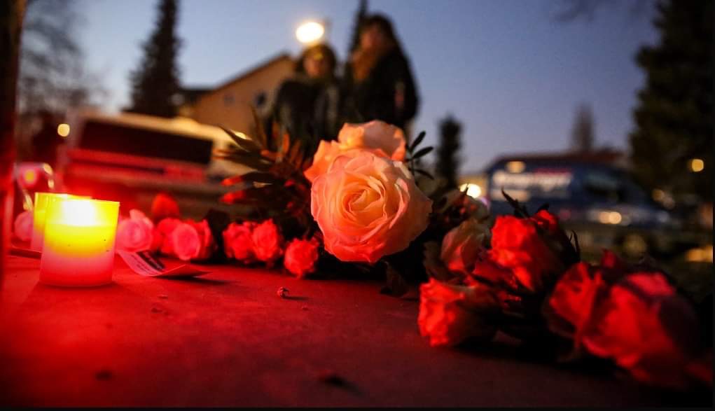 Foto: Montag, 14. Februar 2022 / 17:30 Uhr / Gedenkort für Burak Bektaş / Bildbeschreibung: in der Dämmerung auf der Straße niedergelegte Rosen neben Grablicht, im Hintergrund unscharf zu sehen zwei Trauernde